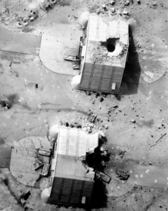 An aerial black-and-white battle damage assessment photograph from Desert Storm, showing two hardened aircraft shelters, one with a large hole in its roof from a direct hit.
